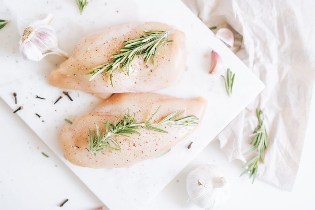 Raw chicken breasts seasoned with rosemary and garlic on a cutting board.